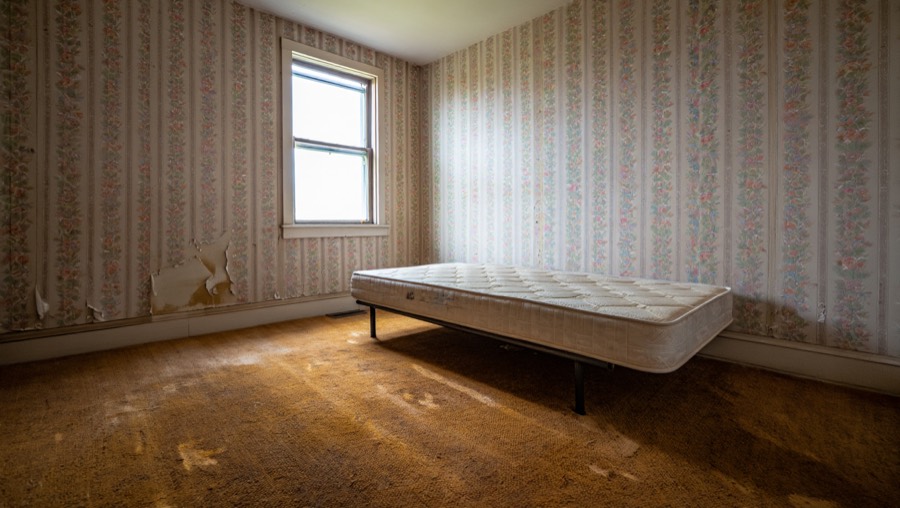 A bedroom before redesign, with faded floral wallpaper and old brown carpet
