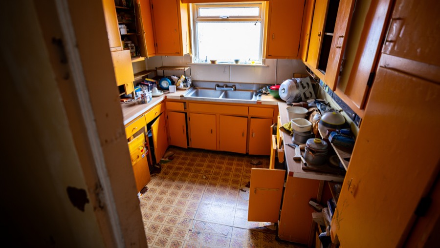 A kitchen before redesign, with 1980s laminate cabinets and worn vinyl flooring