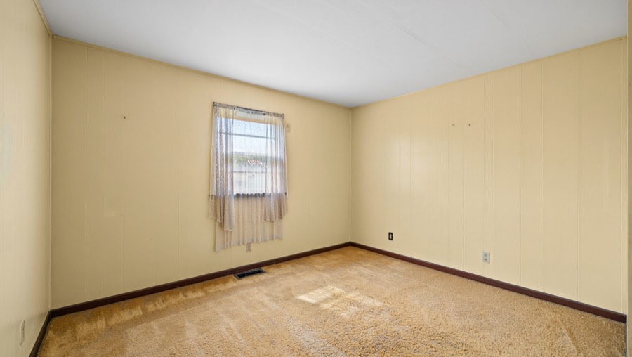 A living room before redesign, with magnolia panelled walls and worn carpet